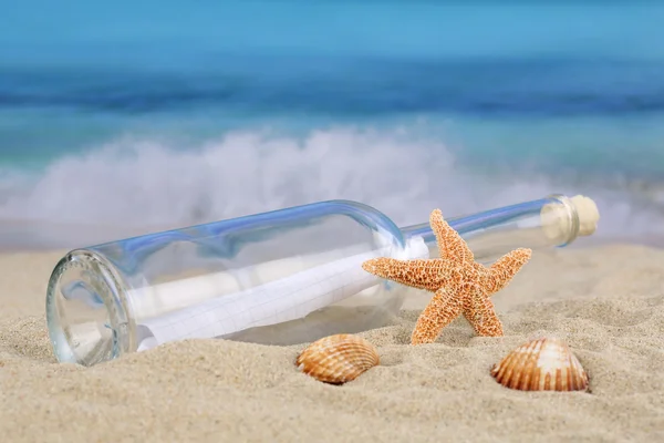 Fles met boodschap op het strand met schelpen en zeester